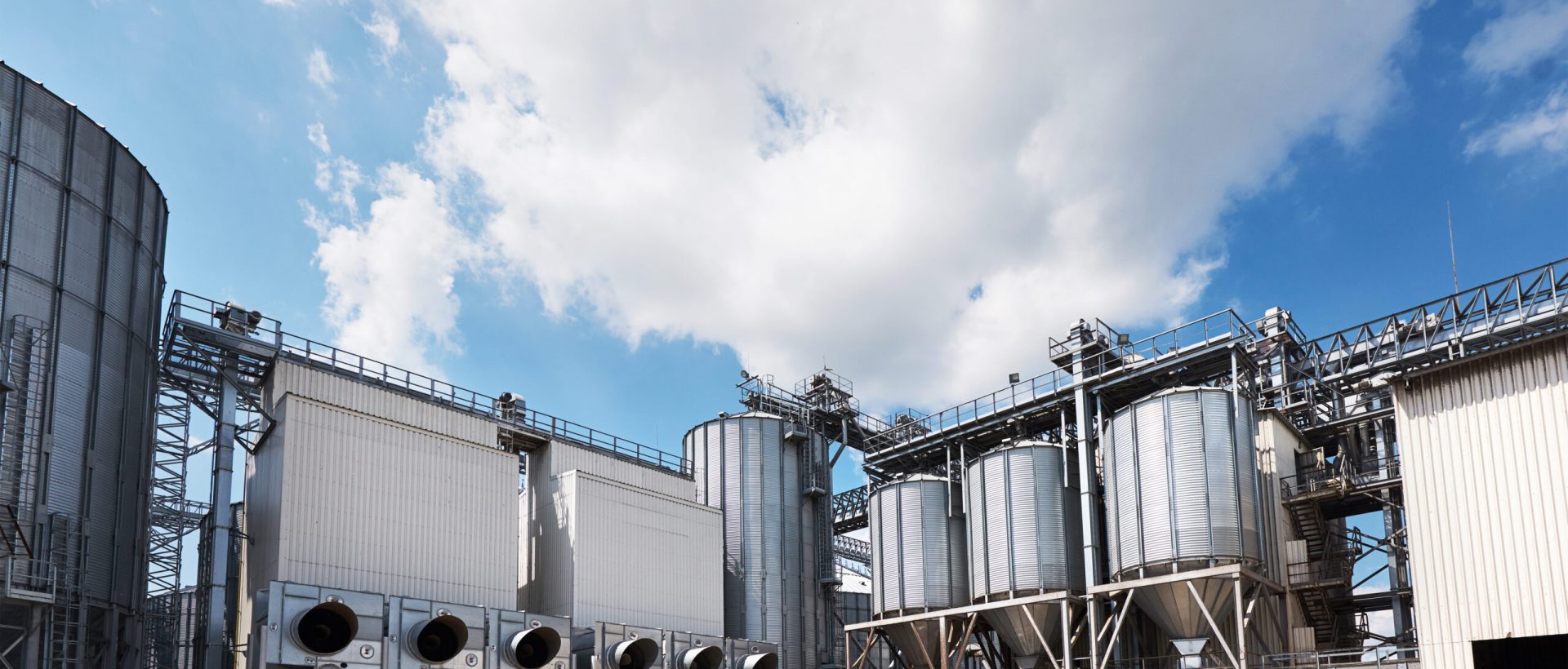 Agricultural Silos. Building Exterior. Storage and drying of grains, wheat, corn, soy, sunflower against the blue sky with white clouds.
